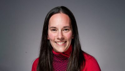 Portrait of Ciji Clark smiling in a red patterned sweater with a neutral gray background