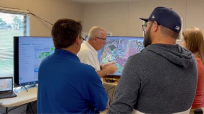 Four people huddle around digital maps on computer screens