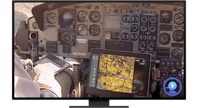 A person sitting at the dashboard of an aircraft with a keyboard and a monitor displaying a map