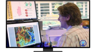 A person looking at two desktop monitors that have a dashboard and digital map displayed