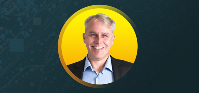 Portrait of Daniel Johns smiling in a dark suit in a sunlit lobby