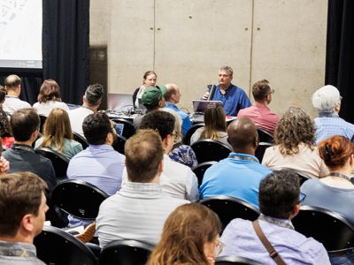 Rows of seated attendees facing two presenters in a Demo Theater