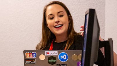 An Esri expert with long dark hair smiles as she gives a demo with her open laptop decorated with tech-related stickers