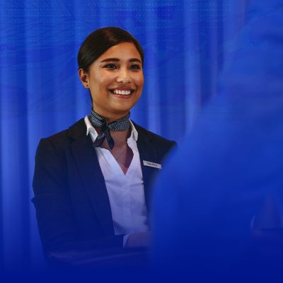 A young woman in professional attire smiles warmly while interacting with a customer