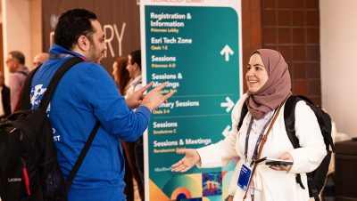 Two conference attendees converse animatedly in a hallway near a large directional sign
