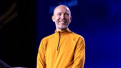 A middle-aged man stands on a stage, smiling warmly at the audience