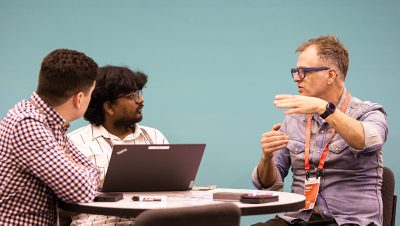 Three men sit around a small round table engaged in an animated discussion