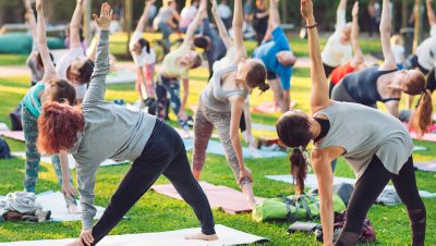 A large group of people practice yoga together on a grassy lawn