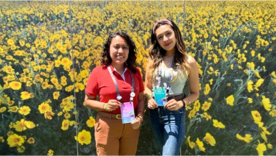 Diana stands in front of a floral wall graphic holding her Esri User Conference badge. 