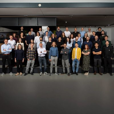 A large group of people wearing business casual clothing standing together in an office and smiling