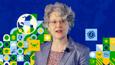 Speaker wearing a microphone in front of a vibrant blue background overlaid with a globe graphics and tech-themed icons