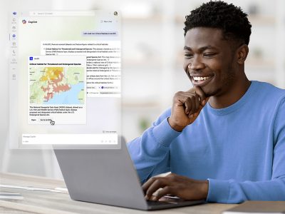 Casually dressed person smiling at an open laptop in a sunlit home office, overlaid with a map display