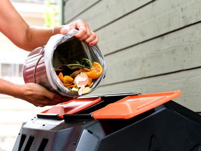 A pair of hands tipping the contents of a small compost bucket into a bin