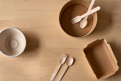 Overhead view of a pale wooden tabletop strewn with biodegradable bowls, cutlery, and takeout containers