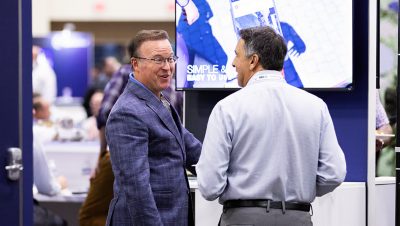 Two people dressed in business attire smile and interact in a busy conference hall