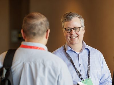 Smiling event attendee wearing a blue dress shirt talking to an Esri expert who has their back to the camera