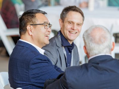 Three seated attendees wearing suits smiling and interacting