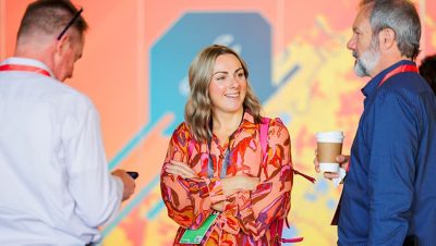 Three people wearing business attire talking and smiling against a colorful backdrop