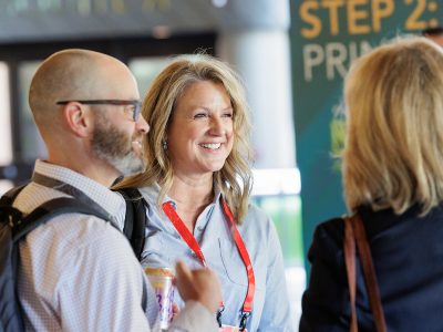 Smiling Esri employee with a red event lanyard talking to two attendees