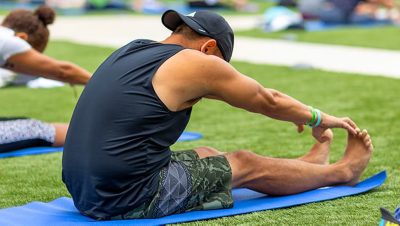 Person stretching forward to touch their toes on a yoga mat outside on a grass lawn