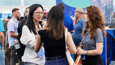 A small group of conference attendees in the Expo area, with one listening intently