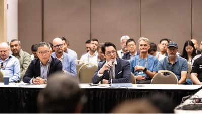 A group of professionals sit at a long table speaking into microphones during a conference panel discussion