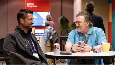 Two middle-aged men sit at a round table, engaged in a friendly conversation at a professional conference
