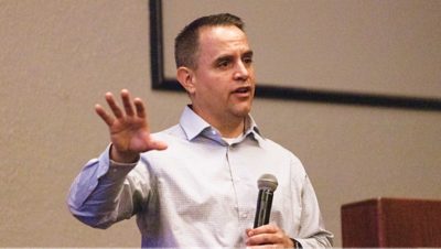 A man stands indoors giving a presentation while holding a handheld microphone