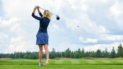 A woman golfer is captured from behind as she swings a driver on a lush green fairway