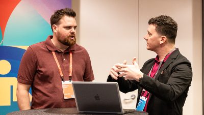 Two men stand at a small round table engaged in a focused conversation at a conference or networking event 