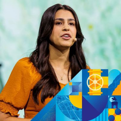 Speaker wearing a headset microphone and orange blouse with long dark hair