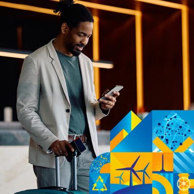 Person in business casual attire looking at their smartphone and holding the handle of a roller suitcase