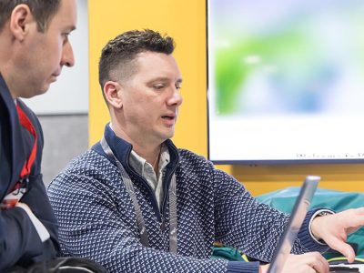 Attendee wearing a lanyard seated at a laptop talking to an Esri expert