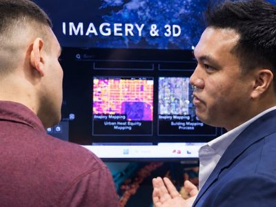 Two people talking with a sign labeled "Imagery and 3D" and a urban heat equity map in the background