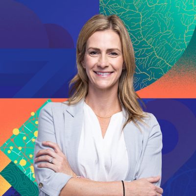Portrait of a person with arms crossed in front of a colorful abstract background featuring map-like patterns