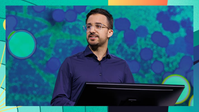 Presenter standing behind a monitor with a large abstract map-style graphic displayed in the background