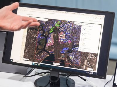 Close-up of a computer monitor displaying a satellite map with a hand pointing to a highlighted area