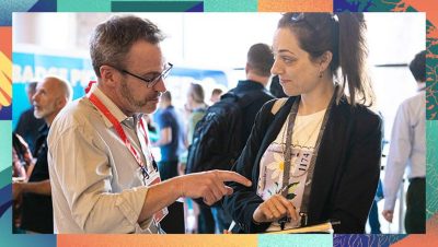 Two attendees standing and discussing content with one pointing to a device