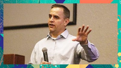 Conference speaker holding a microphone and gesturing while presenting in front of a screen
