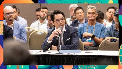 Seated attendee speaking into a microphone during a session with other attendees listening in the background