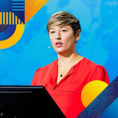 Conference presenter onstage with a blurred map background and colorful abstract geometric elements framing the corners