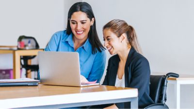 Two people looking at a laptop and smiling with one seated in a wheelchair