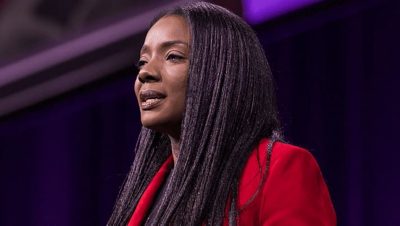 Speaker with long hair looks to the right during a presentation