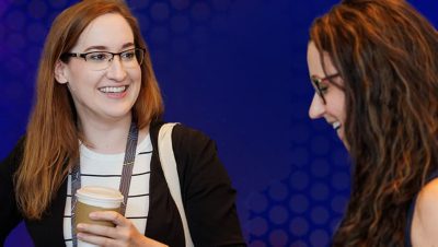 Distributor holding a paper coffee cup smiles at another summit attendee