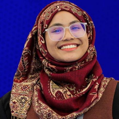 Portrait of a smiling person wearing large glasses and a headscarf in a brown pattern
