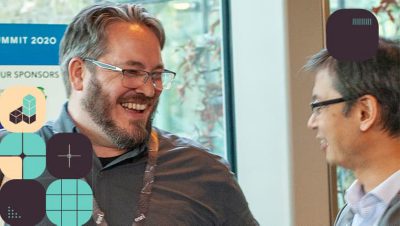 Two smiling attendees wearing glasses and business casual attire engaged in conversation