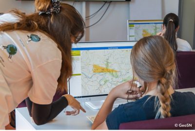 Personen arbeiten an Computern mit einer digitalen Kartenanwendung und analysieren geografische Daten auf einer interaktiven Karte.