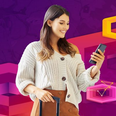 Smiling person wearing a knit sweater glancing down at their smartphone and holding a suitcase handle