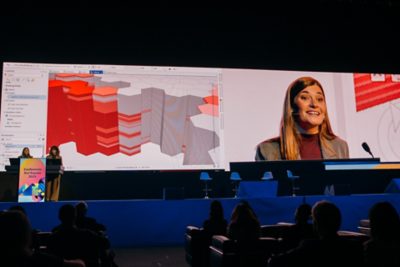 Esri expert wearing a tan suit looking over the shoulder of a seated attendee working on a laptop