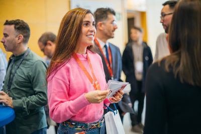Smiling attendees embrace with one wearing a plaid shirt and Esri swag buttons and the other wearing a backpack